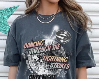 May include: Dark gray t-shirt with the text "Dancing Through The Lightning Strikes Onyx Night" and a disco ball graphic. The shirt has a vintage, worn look and a relaxed fit. The shirt is a unisex style.