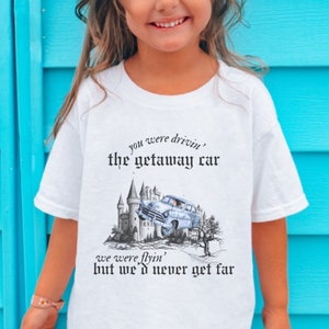May include: White t-shirt with a black graphic print of a car driving away from a castle. The text on the shirt reads "you were drivin' the getaway car we were flyin' but we'd never get far".