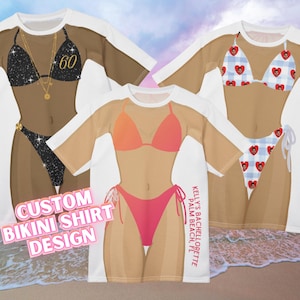 Peut inclure: Trois modèles de t-shirts personnalisés avec des bikinis. Un t-shirt présente un bikini noir à paillettes avec un collier doré et le chiffre 60. Un autre t-shirt a un bikini rouge et orange. Le troisième t-shirt a un bikini à motifs de cœurs bleus et blancs.