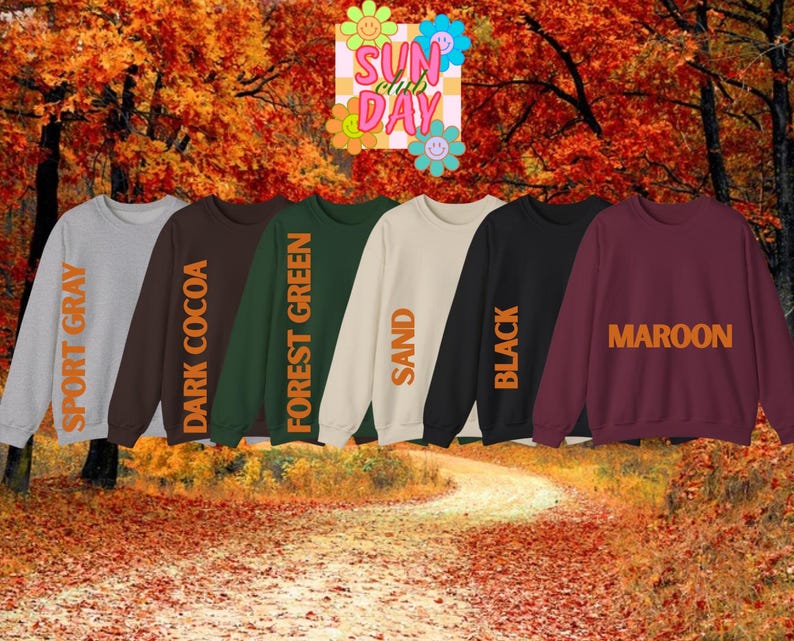 K&ouml;nnte beinhalten: Sechs Rundhals-Sweatshirts in Sportgrau, Dunkelkakaobraun, Waldgr&uuml;n, Sand, Schwarz und Kastanienbraun. Jedes tr&auml;gt den Farbnamen in orangefarbenem Text. Dar&uuml;ber befindet sich eine Grafik mit dem Text SUN CLUB DAY und bunten Blumen.