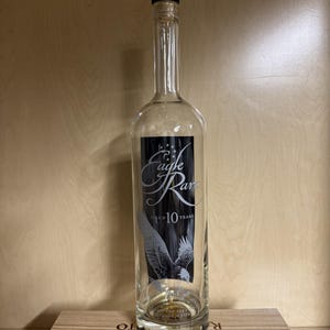 May include: A clear glass bottle with a black cap and a label featuring the words "Eagle Rare" and an illustration of an eagle. The label also indicates "Aged 10 Years". The bottle is displayed on a wooden crate.