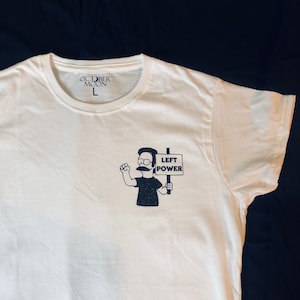 May include: White t-shirt featuring a black and white illustration of a cartoon character holding a sign that reads "LEFT POWER". The shirt has a tag that says "OCTOBER MOON L".