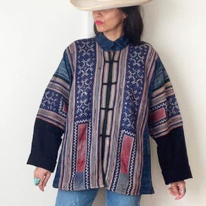 May include: A blue and red patterned jacket with a white collar and black sleeves. The jacket has a button closure and is worn over a pair of blue jeans.
