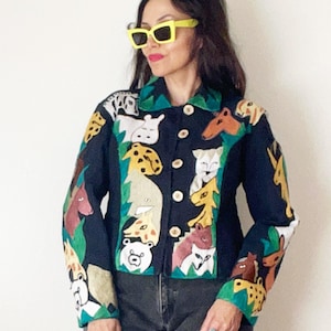 May include: A black long-sleeve jacket featuring a colorful array of animal illustrations including bears, giraffes, and horses. The jacket has a collared neckline, a front button closure with light-colored buttons, and green leaf-like accents.