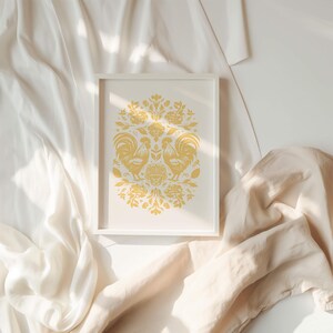 A framed November birth flower art print featuring two stylized green birds and intricate floral patterns is placed on a soft, cream-colored fabric background with gentle folds and light streaming in from one side.
