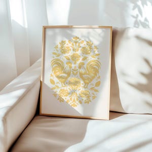 A framed artwork featuring a symmetrical design with two birds facing each other, surrounded by flowers, leaves, and intricate patterns. The piece rests on a light-colored cushioned sofa in a bright room. This November birthday gift exudes charm.