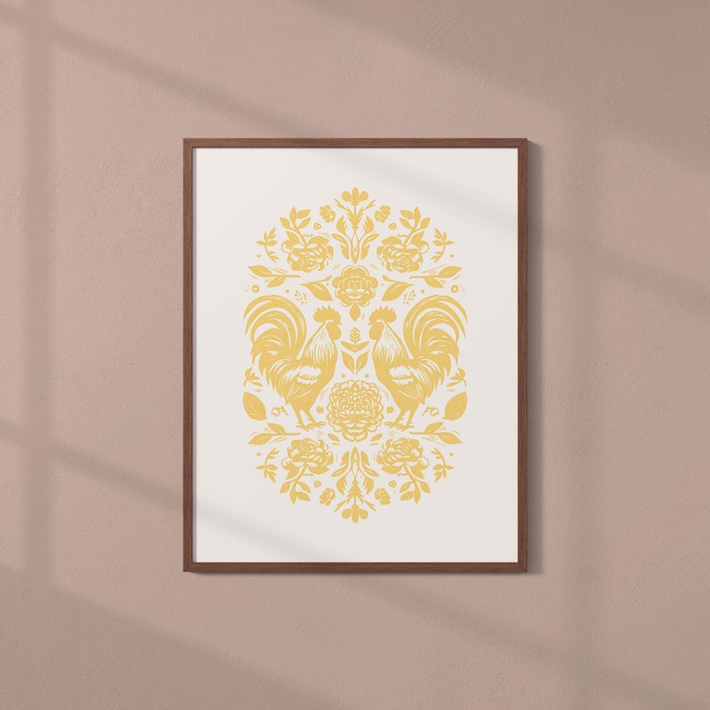 A framed artwork with a symmetrical design featuring two roosters and flowers in yellow on a white background. The wooden frame hangs elegantly on a light brown wall.