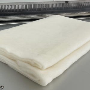 May include: A white, folded piece of fabric. The fabric is soft and fluffy, and it appears to be made of cotton.