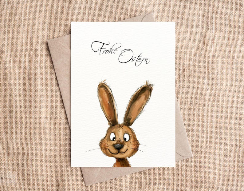 Pu&ograve; includere: Un biglietto bianco con il testo "Frohe Ostern" scritto in corsivo nero. Un coniglio dei cartoni animati con la pelliccia marrone e gli occhi grandi spunta dal fondo del biglietto.