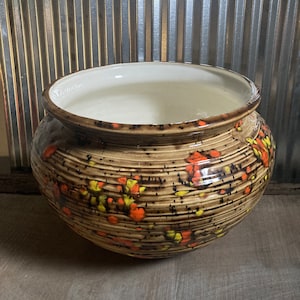 May include: A large, round ceramic planter with a brown, textured glaze. The planter is decorated with a pattern of orange, yellow, and black flowers.