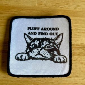 May include: White patch with black border featuring a black and white illustration of a cat with the text "FLUFF AROUND AND FIND OUT".