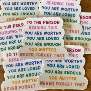 May include: A collection of white die-cut stickers featuring the multi-colored text: TO THE PERSON READING THIS YOU ARE WORTHY YOU ARE LOVED YOU ARE ENOUGH YOU MATTER NEVER FORGET THAT. The stickers are arranged in a scattered overlapping pattern.