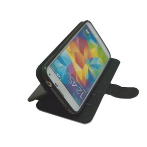 May include: A black leather phone case with a flap that folds over the screen. The case is designed to hold a smartphone and has a built-in stand for hands-free viewing. The phone case is shown with a white smartphone inside.