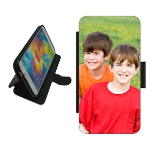 May include: Black smartphone case with a photo of two smiling children in red and orange shirts. The phone is displayed with a colorful screen. The case is open, revealing the phone's screen and a stand.