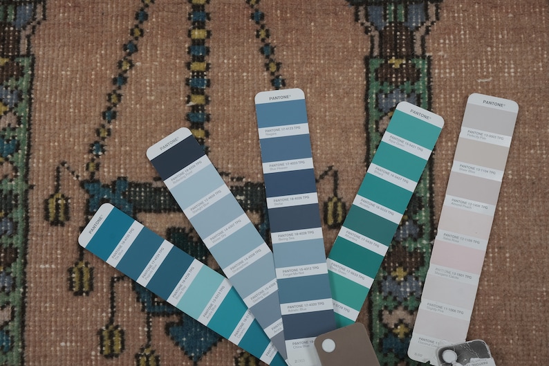 May include: A close-up of six Pantone color swatches, showing various shades of blue and teal. The swatches are laid out on a patterned rug.