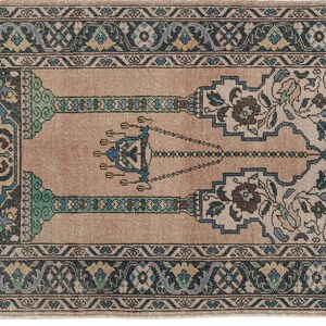 May include: A beige prayer rug with a traditional design featuring a central chandelier motif and floral patterns in shades of blue, green, and brown. The rug has a border with intricate geometric designs.