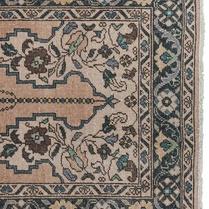 May include: A vintage rug with a beige background and a dark blue border. The rug features a floral pattern with intricate details.