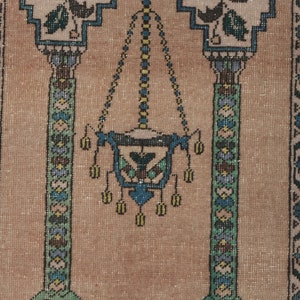 May include: A beige prayer rug with a traditional design featuring two pillars with floral motifs and a hanging lamp in the center. The rug has a detailed pattern with blue, green, and yellow accents.