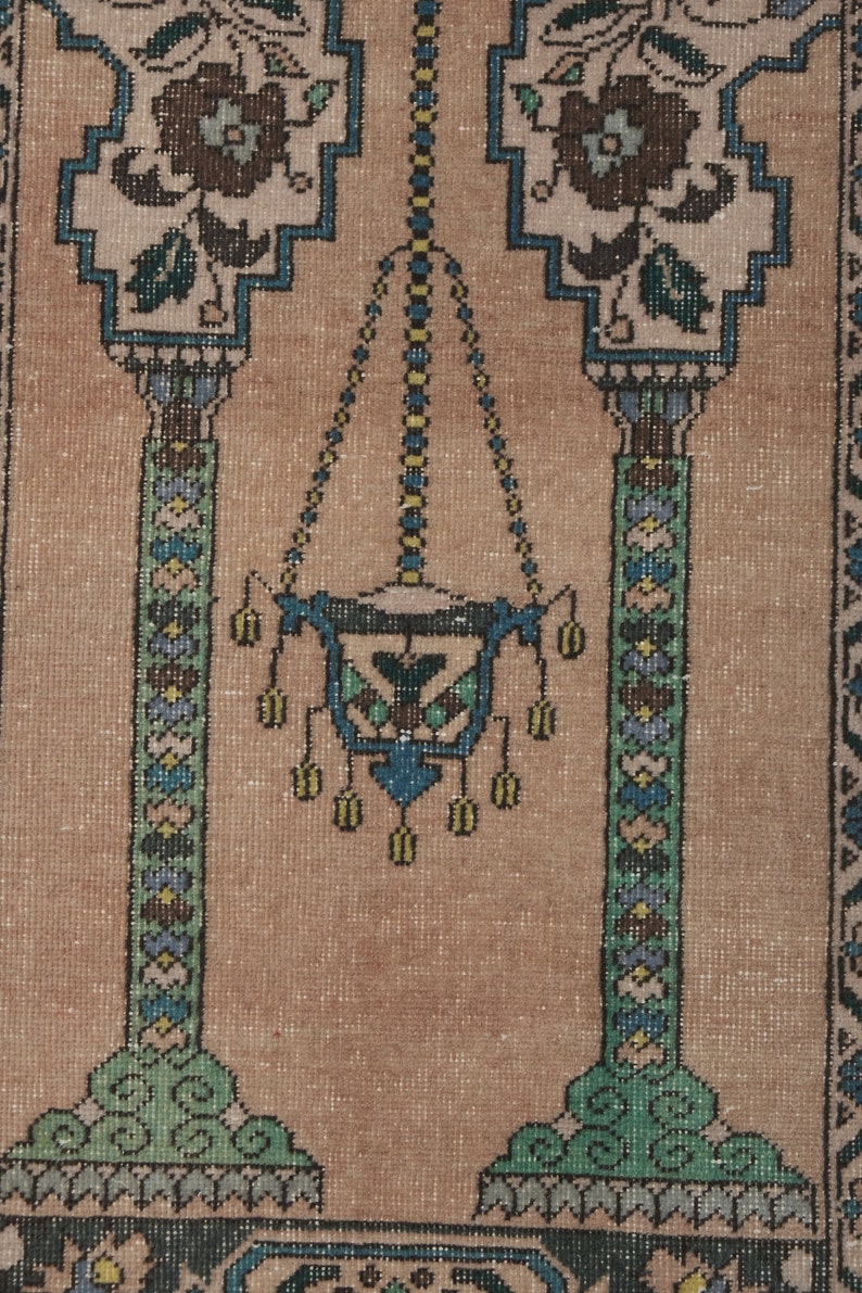 May include: A beige prayer rug with a traditional design featuring two pillars with floral motifs and a hanging lamp in the center. The rug has a detailed pattern with blue, green, and yellow accents.