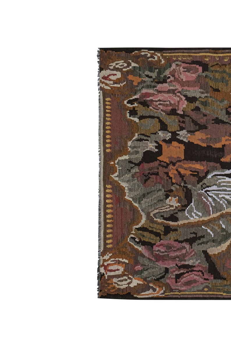 Op de afbeelding: Een fragment van een geweven tapijt met een bloemenpatroon. Het tapijt heeft een kleurenpalet van bruin, roze, groen en oranje. De randen hebben een gefranjerde rand. Het ontwerp van het tapijt omvat gestileerde bloemen en bladeren.
