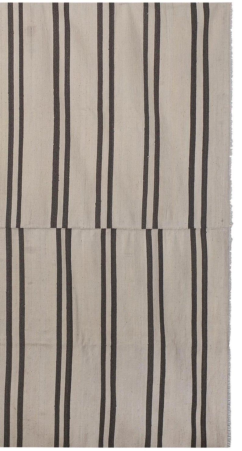 May include: A white and black striped rug with a woven texture. The rug has a fringe border.