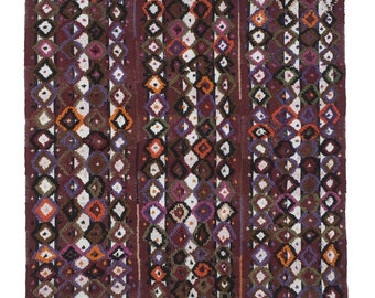 Peut inclure: Un tapis vintage avec un motif géométrique dans des tons de brun, blanc, orange, violet et vert. Le tapis a une bordure à franges.