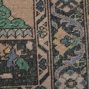 May include: Close-up of a rug with a beige background and a dark blue border. The border features a floral pattern with yellow, green, and blue accents.