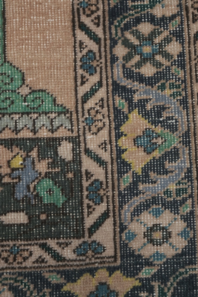 May include: Close-up of a rug with a beige background and a dark blue border. The border features a floral pattern with yellow, green, and blue accents.
