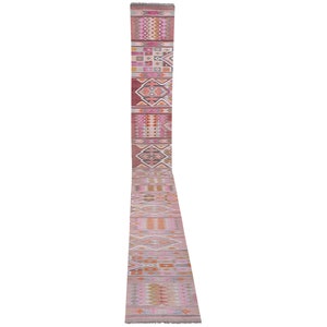 Puede incluir: Una alfombra larga y estrecha con un patrón geométrico rosa, naranja y blanco. La alfombra tiene flecos en ambos extremos.