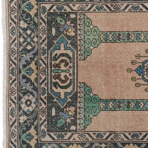 May include: A vintage rug with a beige background and a dark blue, green, and cream patterned border. The rug has a traditional design with floral motifs and geometric shapes.
