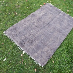 May include: A gray and brown wool rug with a white fringe border. The rug is laid out on a green grassy surface.