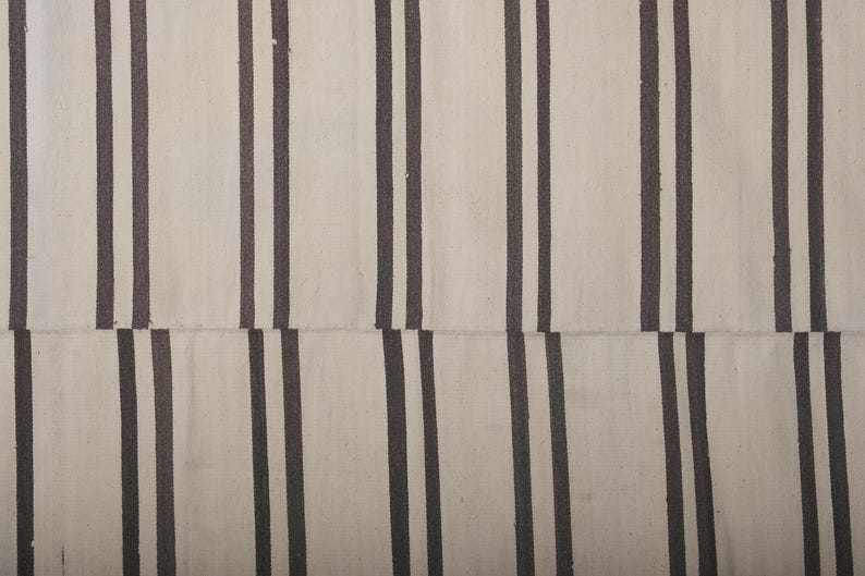 May include: A white and black striped rug with a woven texture. The rug has a simple design with alternating stripes of white and black.