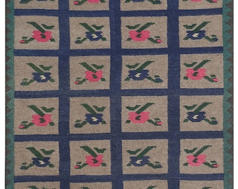 Peut inclure: Un tapis à motifs bruns et bleus avec un motif répétitif de fleurs roses et bleues. Le tapis a une bordure frangée.