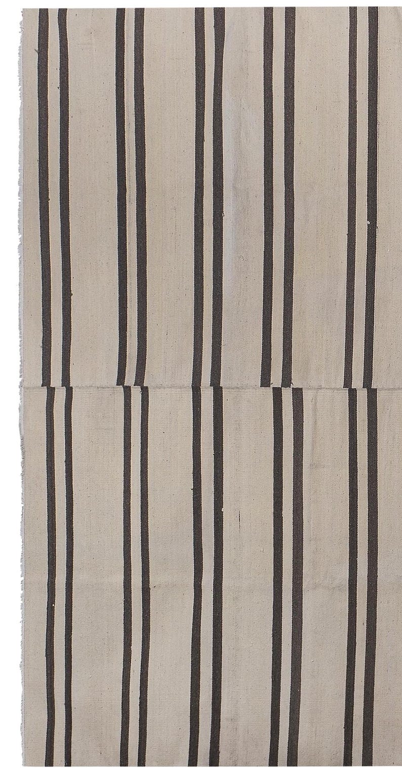May include: A white and black striped rug with a woven texture. The rug is made of natural fibers and has a simple, minimalist design.
