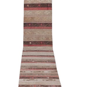 May include: A long, rectangular runner rug with a faded, vintage appearance. The rug features alternating stripes of beige, brown, and red, with geometric patterns. The rug is likely made of woven material.