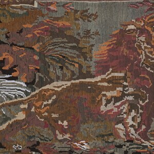 Op de afbeelding: Een geweven tapijt met een landschapssc&egrave;ne. Het tapijt heeft een donkerbruine rand en toont bomen, bladeren en een rivier in bruin-, rood- en groentinten. Het is een decoratief item.