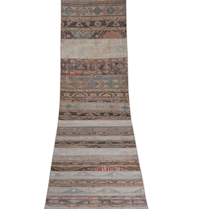 May include: A long, rolled-up runner rug with a distressed, vintage appearance. The rug features a patchwork design with various patterns and colours, including beige, brown, and blue. The rug's dimensions are not visible.