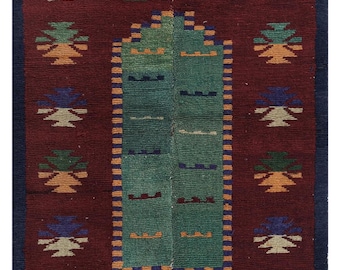 Peut inclure: Tapis rectangulaire tissé à la main, avec un champ rouge foncé. Le tapis présente un motif central vert et des motifs floraux répétés dans des tons de bleu, orange et vert. La bordure est bleu foncé et le tapis a une bordure frangée.