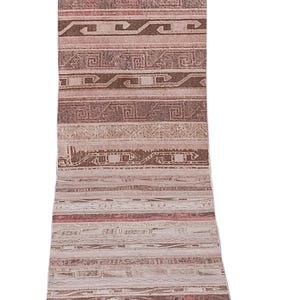 Pode incluir: Um tapete corredor retangular com uma aparência desbotada e vintage. O tapete apresenta um padrão repetitivo de formas geométricas e listras em tons de bege, marrom e vermelho. O design do tapete lembra padrões tribais tradicionais.