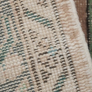 May include: Close-up of a beige rug with a woven pattern of black, green, and blue lines. The rug has a fringe edge.