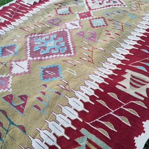 May include: A hand-woven rug with a geometric pattern in shades of red, beige, white, and blue. The rug has a traditional design with intricate details.