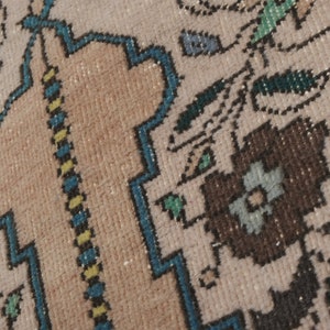 May include: Close-up of a beige rug with a blue, green, and brown floral pattern. The rug has a detailed woven texture.