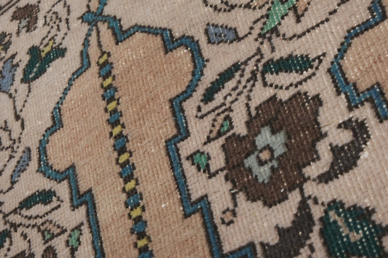 May include: Close-up of a beige rug with a blue, green, and brown floral pattern. The rug has a detailed woven texture.