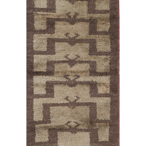 Puede incluir: Una alfombra beige y marrón con estampado geométrico y borde de flecos. La alfombra tiene un diseño tradicional con formas repetidas.