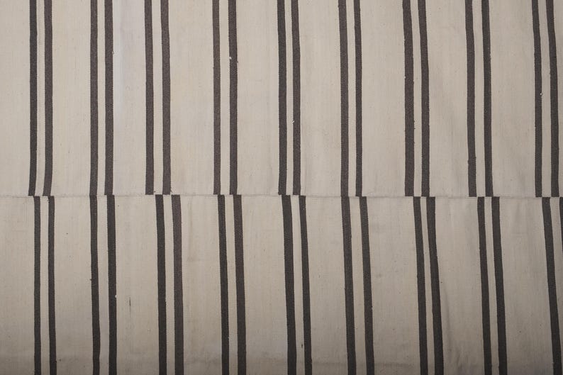May include: A white and black striped rug with a woven texture. The rug has a simple design with alternating stripes of white and black.