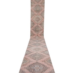 Könnte beinhalten: Ein langer, rosafarbener Läufer mit traditionellem persischem Design. Der Teppich hat ein florales Muster in Grautönen und Braun.