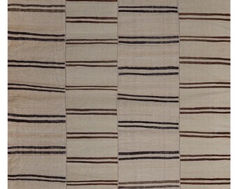 Op de afbeelding: Een beige en bruin gestreept tapijt met een patchwork-ontwerp. Het tapijt is gemaakt van geweven stof en heeft een verweerde uitstraling.