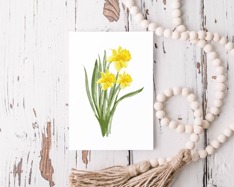 Puede incluir: Una pintura de acuarela de un ramo de narcisos amarillos con hojas verdes sobre un fondo blanco.