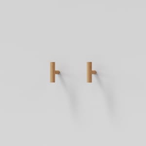 Puede incluir: Dos pomos de armario en forma de T hechos de madera de color claro con un acabado cilíndrico liso. Cada pomo presenta una barra vertical unida a un punto de montaje central, proporcionando un diseño simple y funcional para herrajes de muebles.