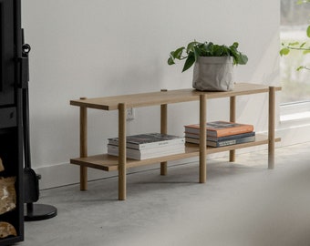 May include: A light wood shelf unit with two shelves, featuring a potted plant and books. The shelf unit is made of natural wood and has a simple, modern design.